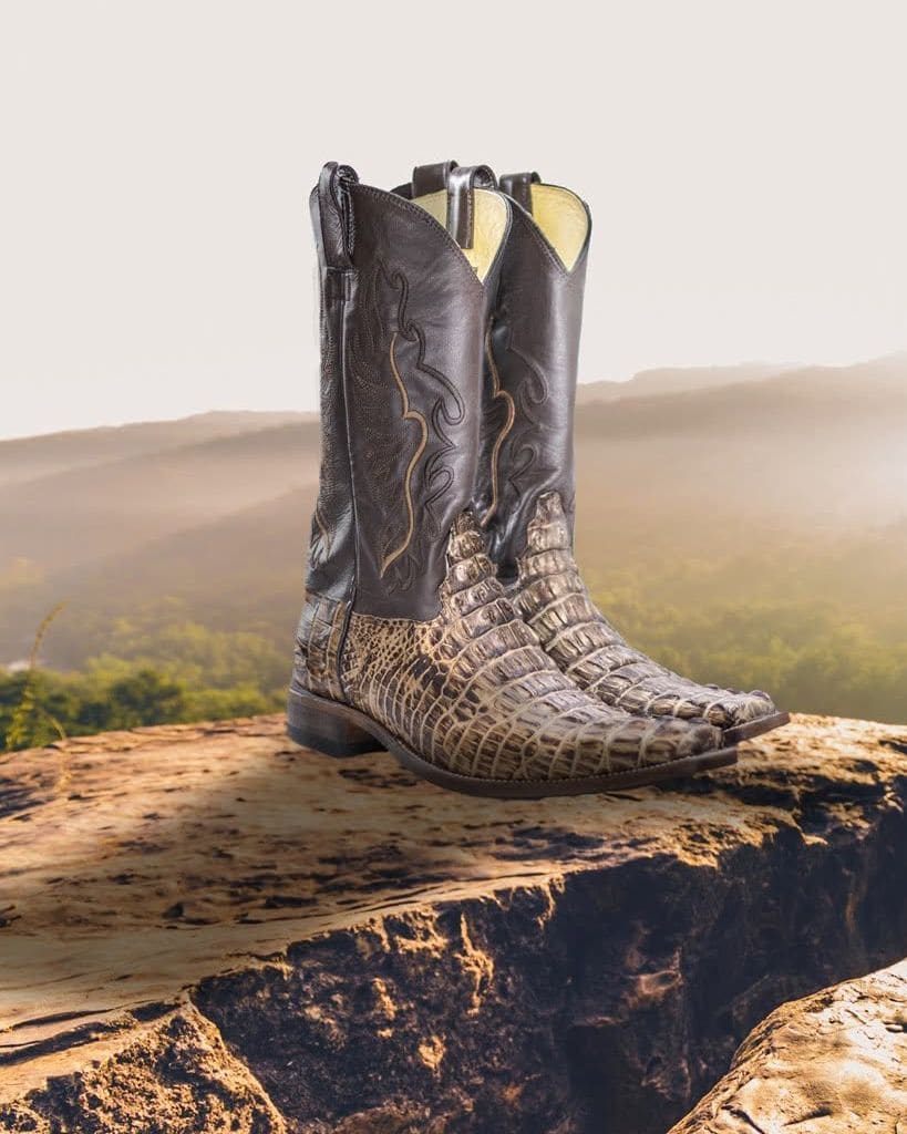 Botas vaqueras de piel exótica sobre una roca, con cerros y niebla al fondo